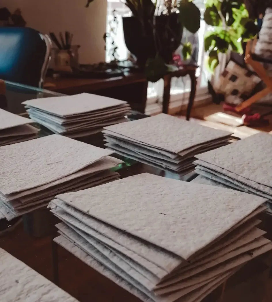 Piles de feuilles de papier recyclé artisanal posées sur une table en verre.