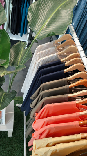 Vêtements colorés suspendus sur cintres en bois dans une boutique, du beige au corail